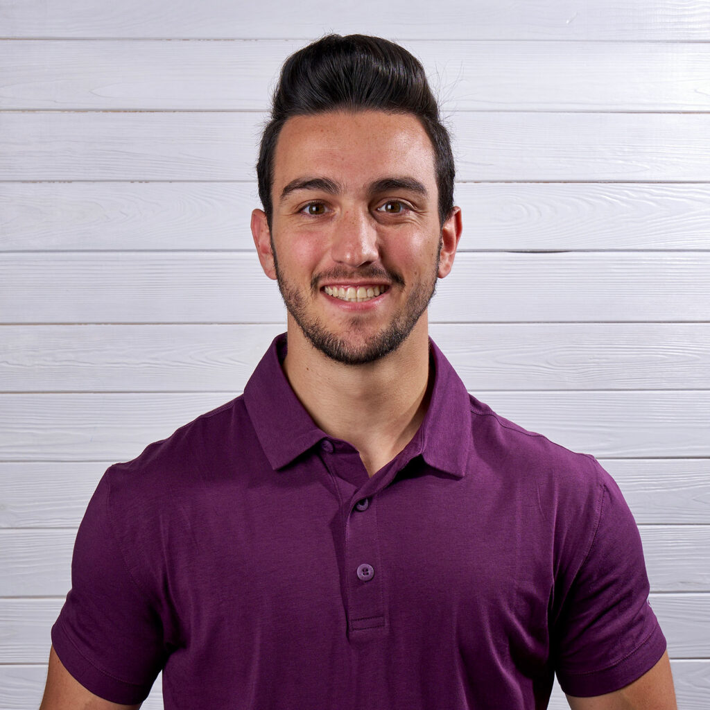 Ethan Kudler smiling and posing in a headshot with a plum purple polo shirt