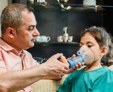 Man helping young girl with asthma inhaler
